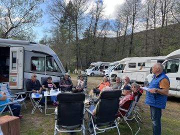 A row of camper vans and motorhomes parked on a gravel path at Farma Sotira, with green trees providing a natural backdrop.